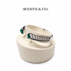 AVENYS & CO. Crossover Bangle in White Gold with green trillion end stones, white pavé panels and dark edging, shown on a cream display holder.